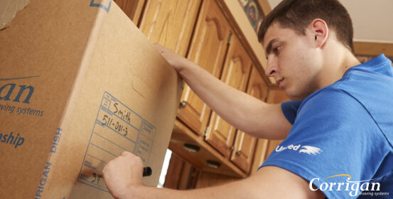 A mover is labeling a cardboard box with a marker in a kitchen. The label reads: "Smith 511-001-3".